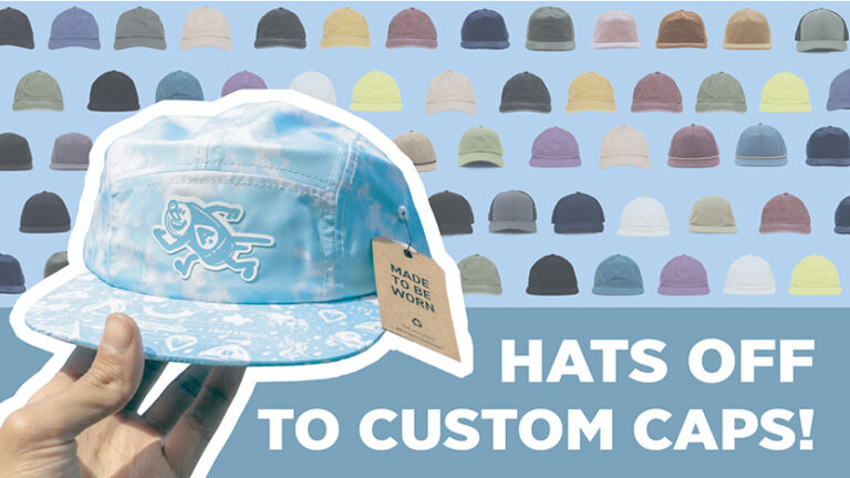 A person holds a light blue cap with a tag reading "Made to be worn." The background features an array of colorful caps in various shades. The text "Hats off to custom caps!" is prominently displayed on the right.