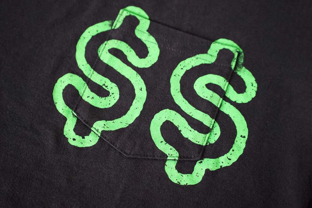 A black fabric with a symmetrical design featuring two bright green, stylized dollar signs, facing each other, positioned around a central pocket.