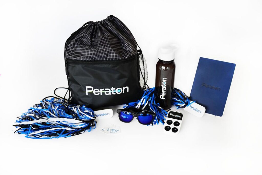 A collection of branded items including a black drawstring bag, pom-poms, a gray water bottle, a blue notebook, sunglasses, a white power bank, and two stickers on a white background. All items feature the Peraton logo.