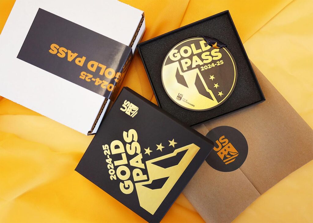 An open box reveals a 2024-25 Gold Pass displayed inside, resting on vibrant yellow fabric. The box lid and envelope beside it are also adorned with the Gold Pass logo and design.