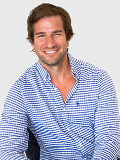 Smiling man with brown hair wearing a blue and white checkered shirt against a light gray background.