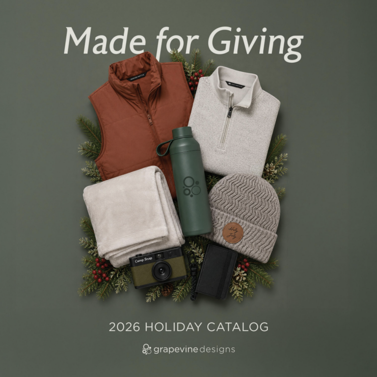 Flat lay of holiday gifts: a rust vest, cream pullover, gray beanie, sage water bottle, cream blanket, camera, and black wallet, surrounded by festive greenery. Text reads “Made for Giving” and “2026 Holiday Catalog.”.